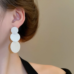 Macro detail of triple silver-tone brushed circular drop earrings on a female model
