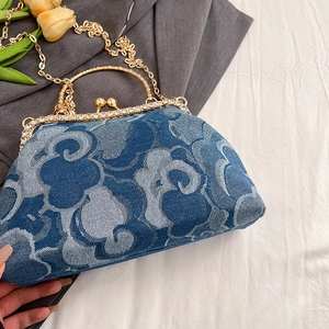 Detail of blue denim kiss-lock handbag with white cloud patterns and rhinestone accents