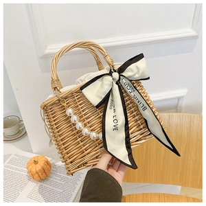 Close-up of woven straw handbag featuring a large ribbon bow and pearl bead handle detail