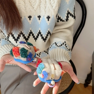 Detailed close-up of a plush beige bucket coin purse featuring blue and pink pom-pom charms