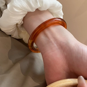 Detail view of a translucent amber resin open bangle on a wrist with soft lighting