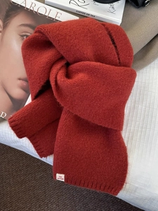 Détail d'une écharpe en tricot à carreaux rouges avec étiquette The Autumn sur lit
