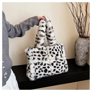 Close-up of fluffy black and white cow print plush handbag held in a minimalist setting