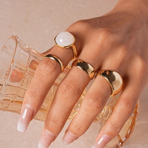 Detail of gold metal rings with white translucent gemstone worn on hand in warm lighting