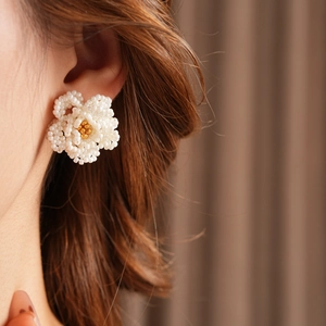 Close-up of white and gold beaded camellia flower earrings worn by a female model