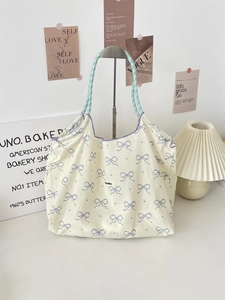 Close-up of cream floral tote bag with purple bow pattern and green woven handle