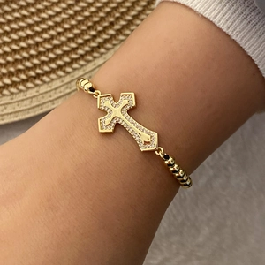 Detailed shot of gold plated cross bracelet with cubic zirconia on woven strap