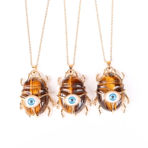 Detailed view of three beetle pendants with brown tiger eye stone and blue evil eye detail