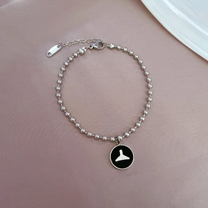 Détail d'un bracelet boule en acier argenté avec pendentif en émail noir sur fond lilas
