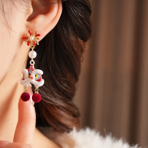 Detail of lion dance earring with white pearl and red pom poms on a model's ear