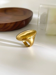 Close-up of a bold gold-plated oval ring with a high-polished finish on white surface
