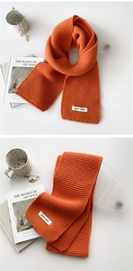 Detailed view of the thick orange knitted scarf with a white woven label on the surface