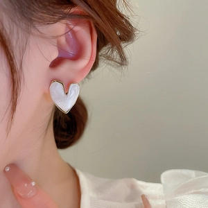 Close-up of minimalist heart-shaped gold earring with white enamel on an ear