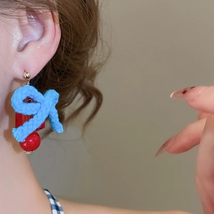 Close-up of dangling resin earrings with blue woven knots and red beads on a model