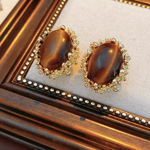 Detailed close-up of vintage gold earrings with oval brown tiger eye stones on fabric
