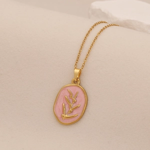 Macro view of a gold-plated necklace featuring a pink enamel oval pendant with olive branch