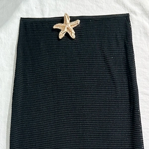 Detail of black mesh sarong with a gold starfish accessory on textured fabric