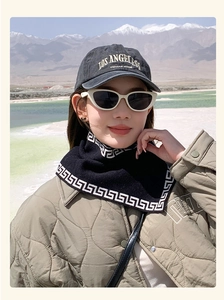 Detail of a black scarf with white Greek key patterns against a snowy mountain backdrop