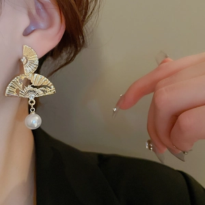 Détail de boucles d'oreilles dorées en forme d'éventail avec perles portées par un mannequin