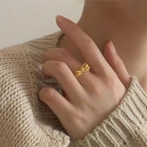 Detail of a minimalist gold bow ring worn on finger with a soft knit sweater background