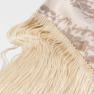 Close-up of golden printed fabric with elegant long fringe tassels and retro floral patterns