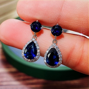 Macro shot of silver-toned pear-cut blue gemstone earrings with white zircon halo