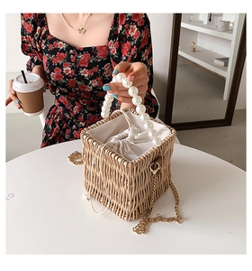 Detail of woven straw bucket bag with large pearl handle and beige drawstring lining