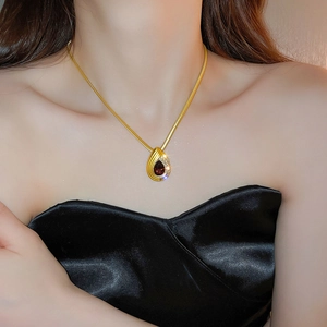Close-up of gold snake chain necklace with ruby teardrop pendant on model's neck