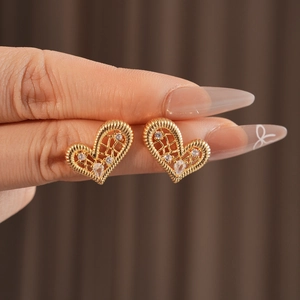 Macro detail of gold-plated heart earrings with woven texture and sparkling zircons