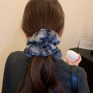 Détail d'un chouchou en tweed à carreaux bleu et gris sur une queue-de-cheval