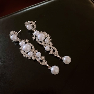 Detail of long drop earrings with white pearls and sparkling rhinestones on black leather