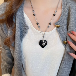 Close-up of gothic black heart pendant necklace with silver cross on grey sweater