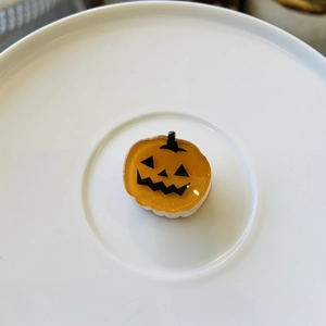Detail shot of a bright orange acetate pumpkin hair claw clip with a classic spooky face