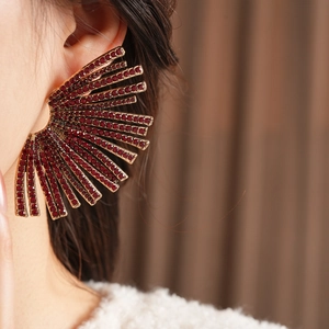 Close-up of luxury fan-shaped rhinestone earrings in wine red and gold on model ear