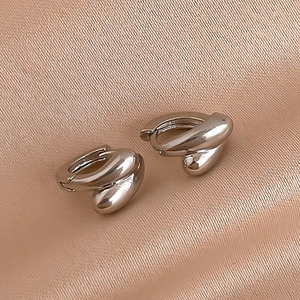Macro shot of silver twisted geometric hoop earrings on soft champagne silk fabric