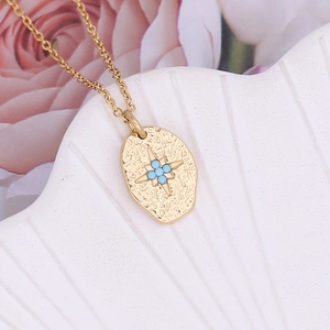 Detail of gold oval textured pendant with turquoise star on a shell and rose background