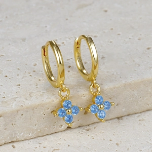 Detailed macro view of gold hoop earrings with four-leaf blue gemstone floral charms