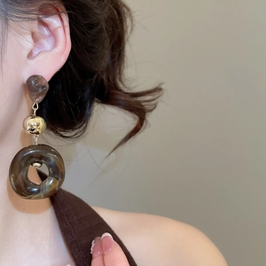 Close-up of marble-textured brown resin and gold bead drop earrings worn by a model
