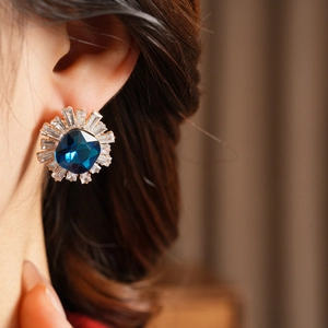 Detailed close-up of a vintage sunburst earring with blue gemstone and baguette zircons