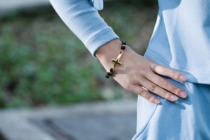 Bracelet à perles noires et croix dorée porté au poignet pour un style bohème chic