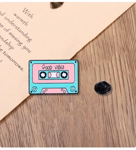 Detail of vintage cassette enamel pin with Good Vibes text on a rustic wooden surface