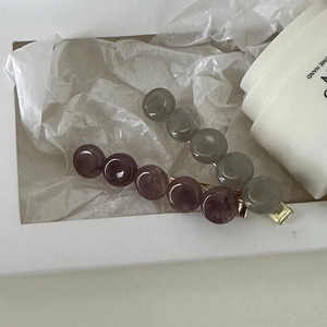 Close-up of gray and burgundy beaded hair clips with gold metal base in a gift box