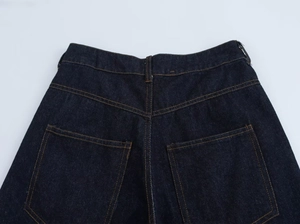 Detail view of deep blue denim pants with orange contrast stitching and rear pockets