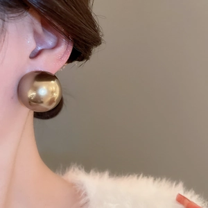 Gros plan d'un mannequin portant de grandes boucles d'oreilles boules dorées au fini miroir
