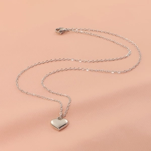 Collier avec pendentif coeur poli en acier inoxydable sur fond de texture en soie douce