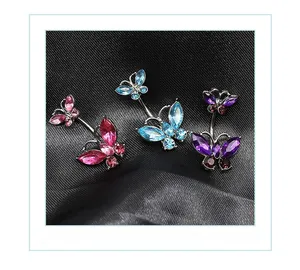 Macro shot of three butterfly navel rings with pink, blue, and purple crystals on velvet