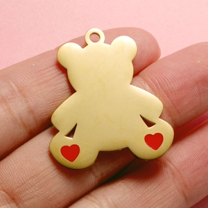 Detailed close-up of a gold bear pendant featuring red hearts, held on a fingertip