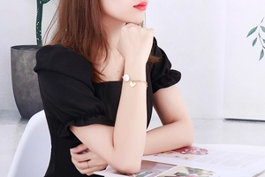 Détail d'un bracelet en chaîne dorée avec perle blanche et pendentif cœur au poignet