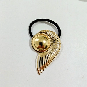 Detailed close-up of golden hollow petal-shaped metal ornament on black elastic hair tie