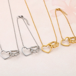 Set aus goldenen und silbernen Herz- und Pfotenketten sowie Armbändern auf rosa Grund